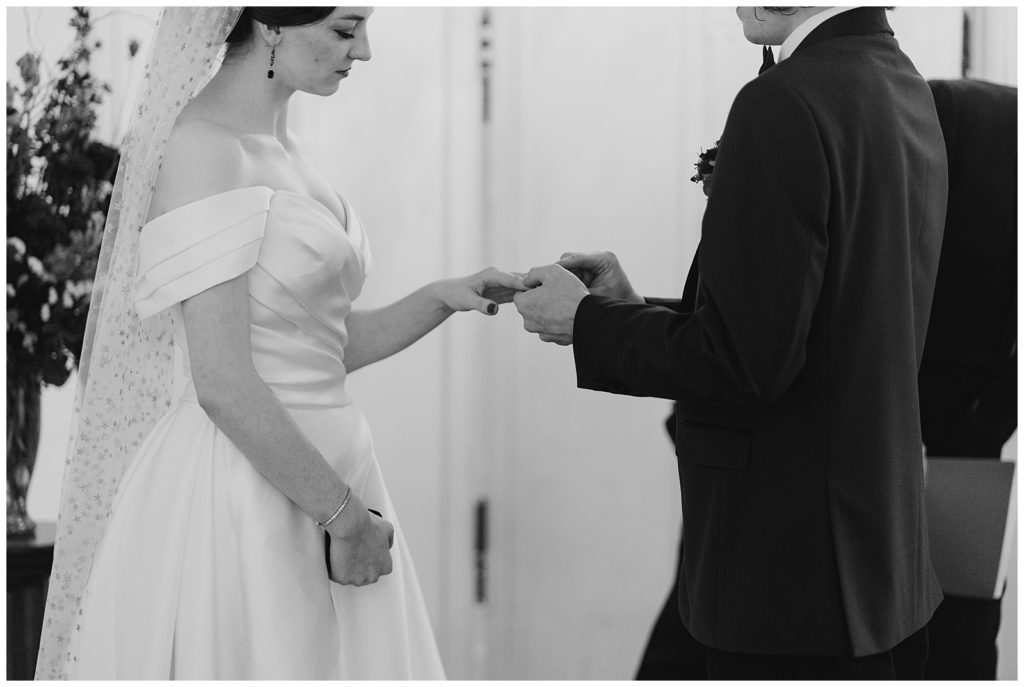 groom places ring on bride's finger in black and white
